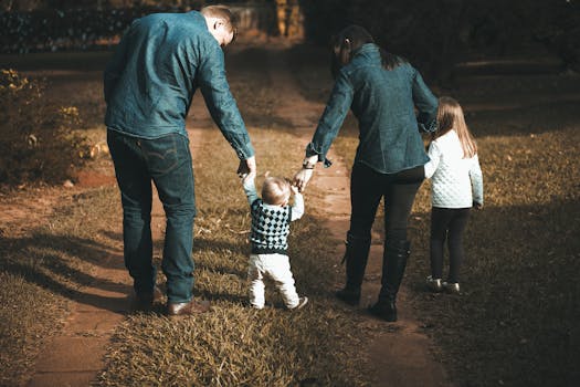 pexels-photo-1682497-1682497 A family of four walks hand in hand on a path, enjoying a sunny day outdoors.